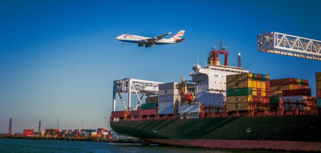 A plane comes in to land over a container ship at a port