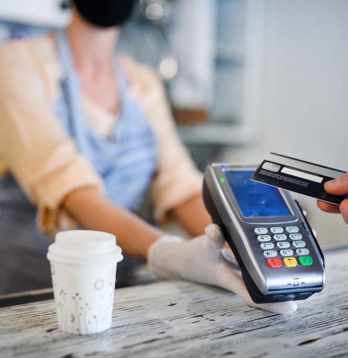 A contactless payment being made over a counter for a drink with the seller wearing PPE mask and gloves