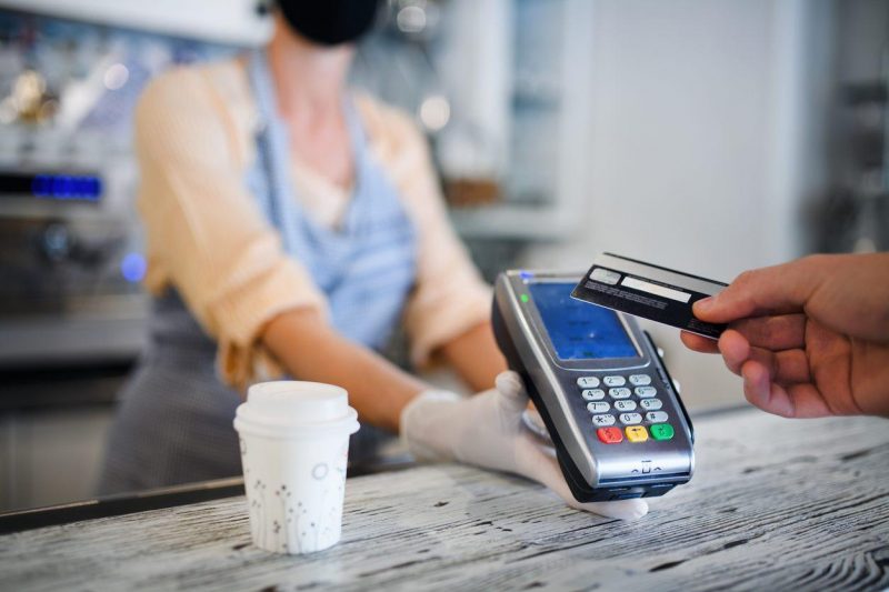 A contactless payment being made over a counter for a drink with the seller wearing PPE mask and gloves