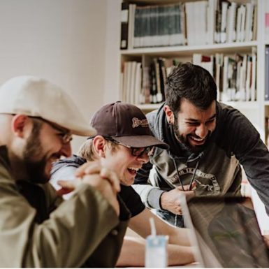 three men smiling and looking a laptop